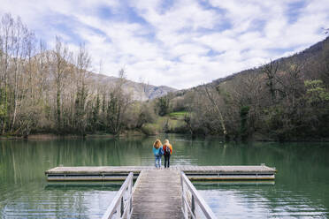 Rückenansicht von zwei Frauen mit Rucksäcken, die auf einem Steg stehen, Stausee Valdemurio, Asturien, Spanien - DGOF00677