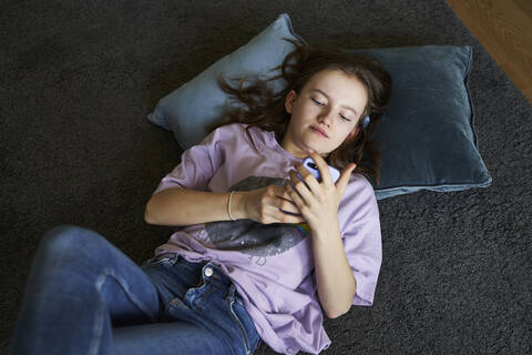 Portrait of girl lying on the floor at home looking at smartphone stock photo