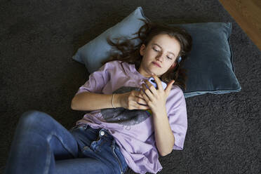 Portrait of girl lying on the floor at home looking at smartphone - AUF00334