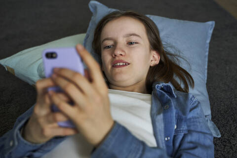 Portrait of girl lying on the floor at home looking at smartphone stock photo