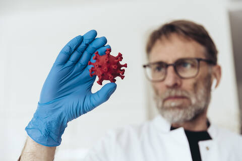 Wissenschaftlerin mit medizinischem Handschuh, die ein Modell des Coronavirus hält, lizenzfreies Stockfoto
