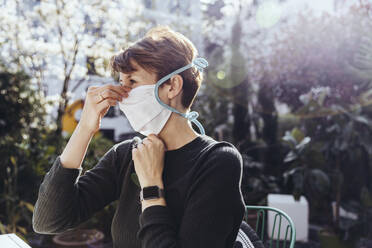 Woman siting in garden, putting on face mask - MFF05386