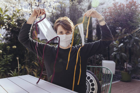 Woman sitting in garden, showing self-made face masks - MFF05388