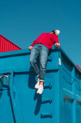 Junger Mann, der sich auf einem blauen Container ausruht und sich nach hinten über den Rand lehnt - ERRF03128