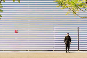 Mann in schwarzem Overall vor einem Industriegebäude stehend - ERRF03149