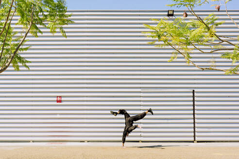Man wearing black overall doing handstand in front of industrial building - ERRF03151