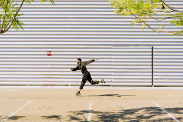 Man wearing black overall jumping in the air in front of industrial building - ERRF03159