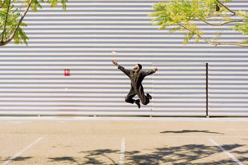 Mann in schwarzem Overall springt vor einem Industriegebäude in die Luft - ERRF03162