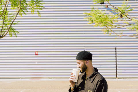 Lächelnder Mann mit Kaffee zum Mitnehmen vor einem Industriegebäude, lizenzfreies Stockfoto