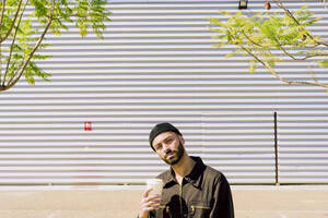 Porträt eines nachdenklichen Mannes mit Kaffee zum Mitnehmen vor einem Industriegebäude - ERRF03168