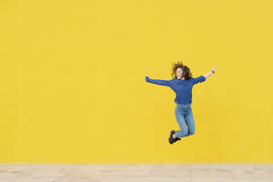 Young woman jumping in the air in front of yellow background - JCZF00031