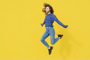 Young woman jumping in the air in front of yellow background - JCZF00032