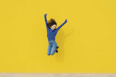 Young woman jumping in the air in front of yellow background - JCZF00039