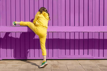 Back view of girl dressed in yellow climbing on bar in front of purple background - ERRF03177