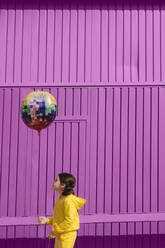 Little girl dressed in yellow holding balloon in front of purple background - ERRF03186