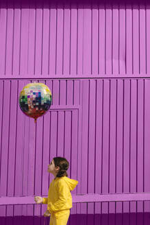 Kleines Mädchen in gelb gekleidet hält Ballon vor lila Hintergrund - ERRF03186