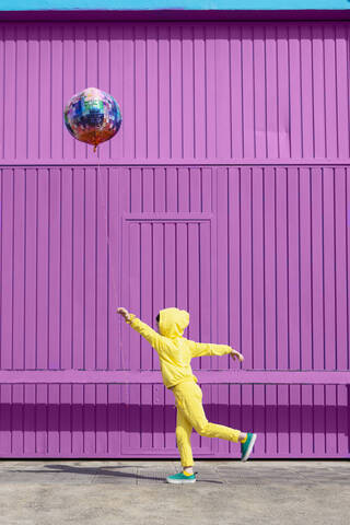 Children dressed in yellow standing in front of purple garage door holding balloon stock photo