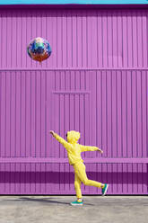 Gelb gekleidete Kinder stehen vor einem lila Garagentor und halten einen Luftballon - ERRF03187