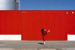 Frau in rotem Overall springt vor rotem Rolltor in die Luft - ERRF03188