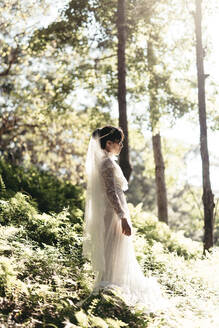 Seitenansicht der Braut stehend inmitten von Pflanzen im Wald - EYF03522