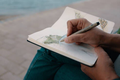 Mittelteil eines Mannes, der in einem Buch auf einem Fußweg skizziert - EYF03637