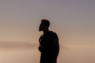 Mann schaut weg, während er bei Sonnenuntergang gegen den Himmel steht - EYF03647