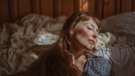 Young Woman With Eyes Closed Leaning On Bed At Home - EYF03700