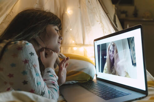 Girl lying on bed at night skyping with her mother working outside home - ERRF03192