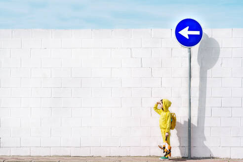 Girl with her cuddly toy at traffic sign, direction left, in front of a white wall - ERRF03211