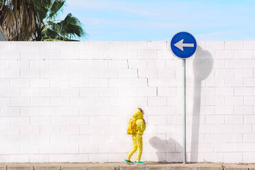 Girl looking at traffic sign, direction left, in front of a white wall - ERRF03214