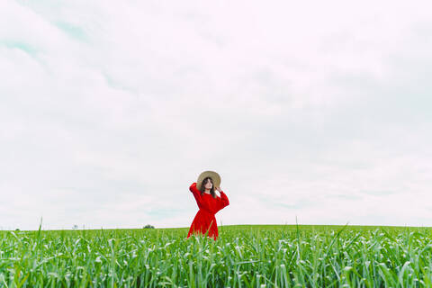 Frau in rotem Kleid und Strohhut auf einem Feld stehend, lizenzfreies Stockfoto