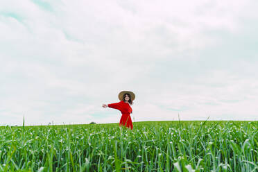 Glückliche Frau in rotem Kleid und Strohhut auf einem Feld stehend - ERRF03220