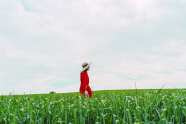 Frau in rotem Kleid und Strohhut geht auf einem Feld - ERRF03221