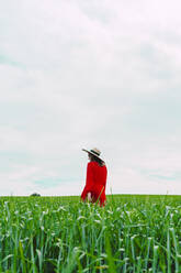 Frau in rotem Kleid und Strohhut geht auf einem Feld - ERRF03222
