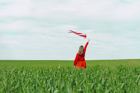Rückenansicht einer Frau im roten Kleid, die einen Windsack auf einem Feld hält - ERRF03225
