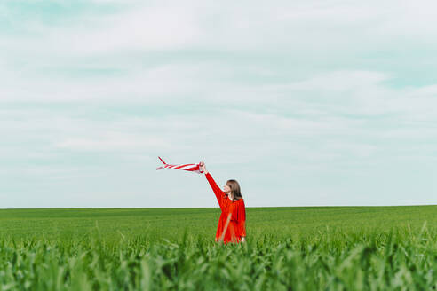 Frau in rotem Kleid steht auf einem Feld und hält einen Windsack - ERRF03226