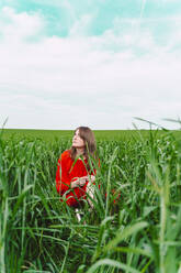 Frau in rotem Kleid sitzt auf einem Feld und schaut nach oben - ERRF03230