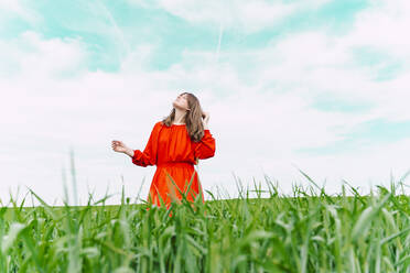 Woman wearing red dress standing in a field with eyes closed - ERRF03232