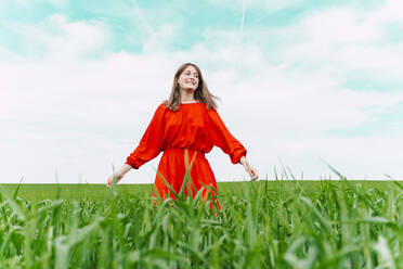 Smiling woman wearing red dress standing in a field - ERRF03235