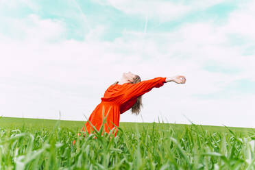 Happy woman wearing red dress relaxing in a field - ERRF03236