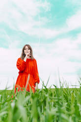 Porträt einer Frau in rotem Kleid, die in einem Feld steht und den Finger auf den Mund legt - ERRF03238