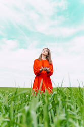 Porträt einer Frau in rotem Kleid, die auf einem Feld steht und nach oben schaut - ERRF03239