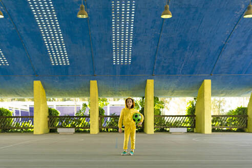 Little girl wearing yellow tracksuit holding soccer ball under her arm - ERRF03246