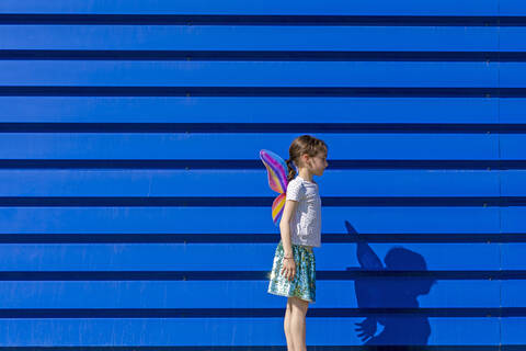 Kleines Mädchen mit bunten Schmetterlingsflügeln vor blauem Hintergrund, lizenzfreies Stockfoto