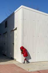 Kleines Mädchen mit rotem Regenmantel versteckt sich hinter einer Ecke - ERRF03268