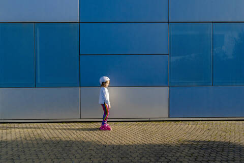 Kleines Mädchen mit Schutzhelm und Inline-Skates bei Sonnenlicht stehend, lizenzfreies Stockfoto