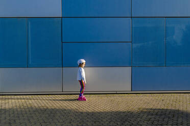 Kleines Mädchen mit Schutzhelm und Inline-Skates bei Sonnenlicht stehend - ERRF03275