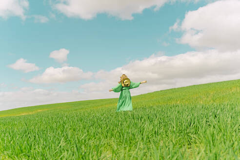 Rückenansicht einer Frau in grünem Kleid, die über ein Feld läuft - ERRF03284