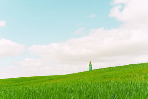 Rückenansicht einer Frau in grünem Kleid, die auf einem Feld steht und in die Ferne schaut, lizenzfreies Stockfoto