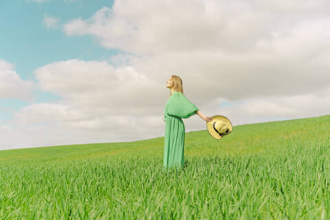 Blonde junge Frau in grünem Kleid steht auf einem Feld, lizenzfreies Stockfoto